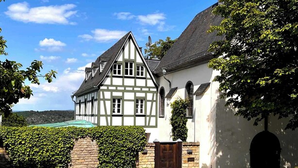 Ett traditionellt hus med korsvirkesfasad, en stenvägg och en trädörr, omgivet av välskötta häckar och en gång av kullersten.