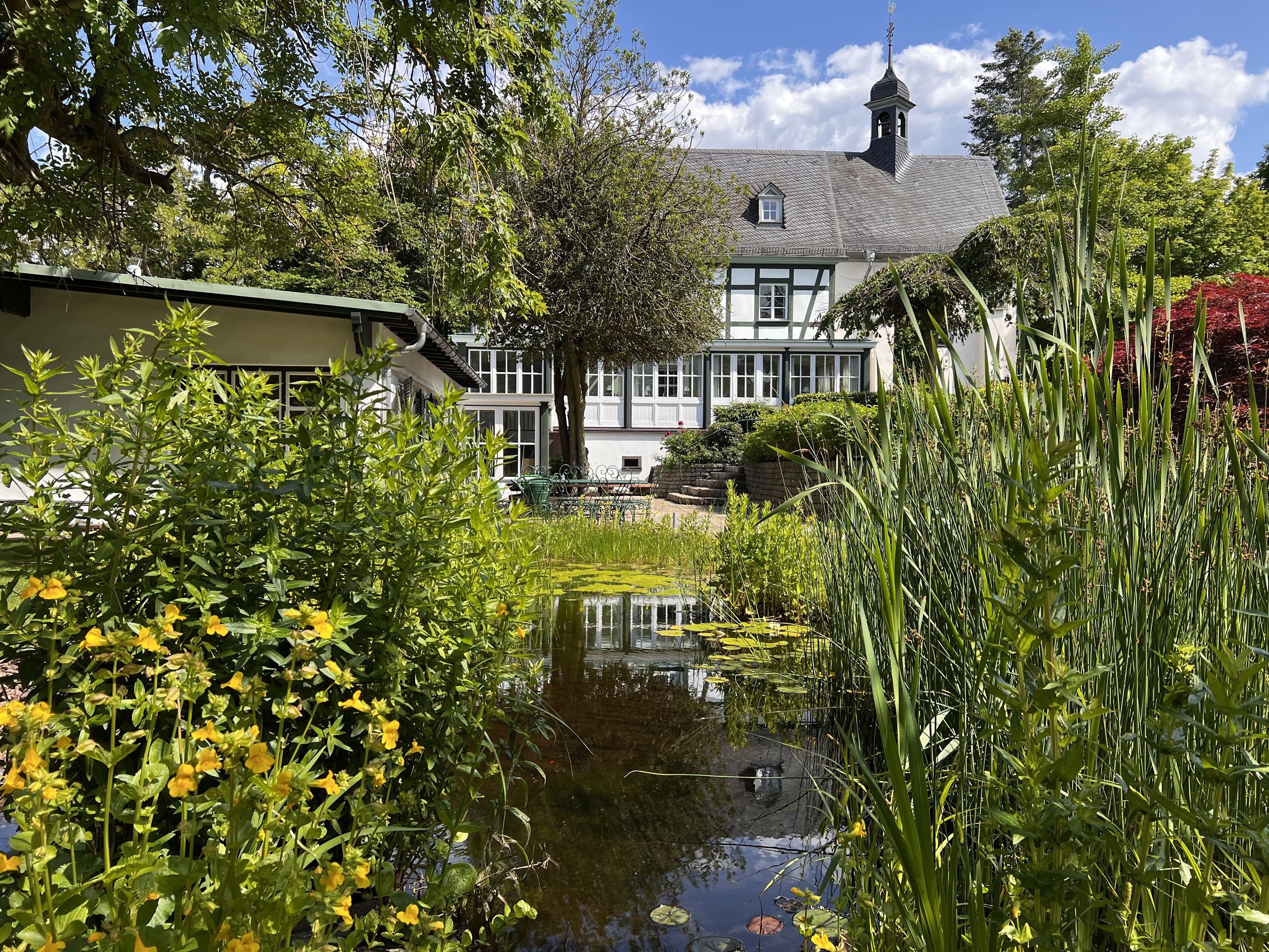 A traditional building with a prominent tower, surrounded by lush greenery and a small pond.