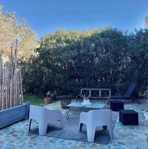Een buitenpatio met stenen vloer, twee witte kunststof stoelen, een tafel en een loungeset.