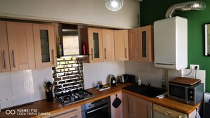 Une cuisine avec des meubles en bois, une cuisinière à gaz, un four à micro-ondes et un mur vert orné d’un tableau.