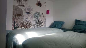Une chambre à coucher avec un lit, deux oreillers et une fresque murale représentant un paysage sous-marin.