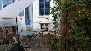 Un espace extérieur aménagé en terrasse, avec une table et des chaises en métal, un parasol blanc et un mur en briques.