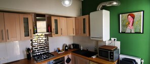A kitchen with wooden cabinets, a gas stove, a microwave, and a green wall with a painting.