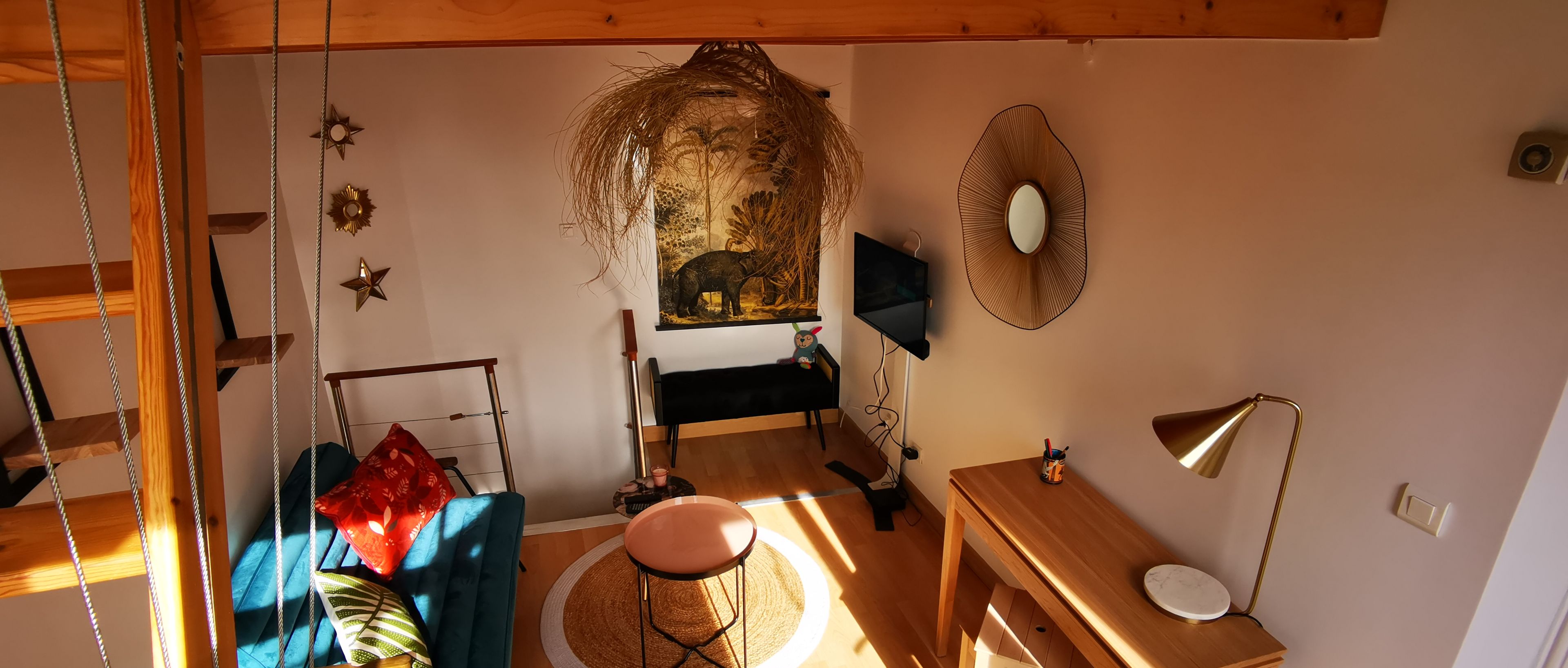 Une pièce chaleureuse avec un canapé bleu, une petite table ronde, un bureau en bois et une plante suspendue.