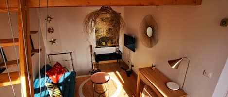 A cozy room with a blue sofa, a small round table, a wooden desk, and a hanging plant.