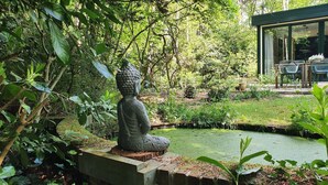 Un jardin agrémenté d’une statue de Bouddha, d’une végétation luxuriante et d’un petit étang.