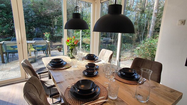 Une table à manger dressée avec des bols et des assiettes noirs, entourée de chaises, et offrant une vue sur la verdure à l’extérieur.