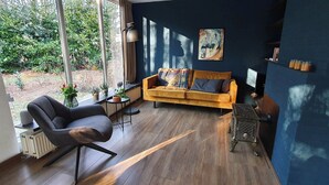 Un salon moderne avec un canapé, un fauteuil, un radiateur et une fenêtre donnant sur un espace verdoyant.