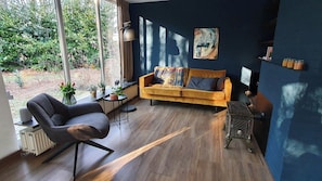 A modern living room with a sofa, a chair, a radiator, and a window overlooking greenery.