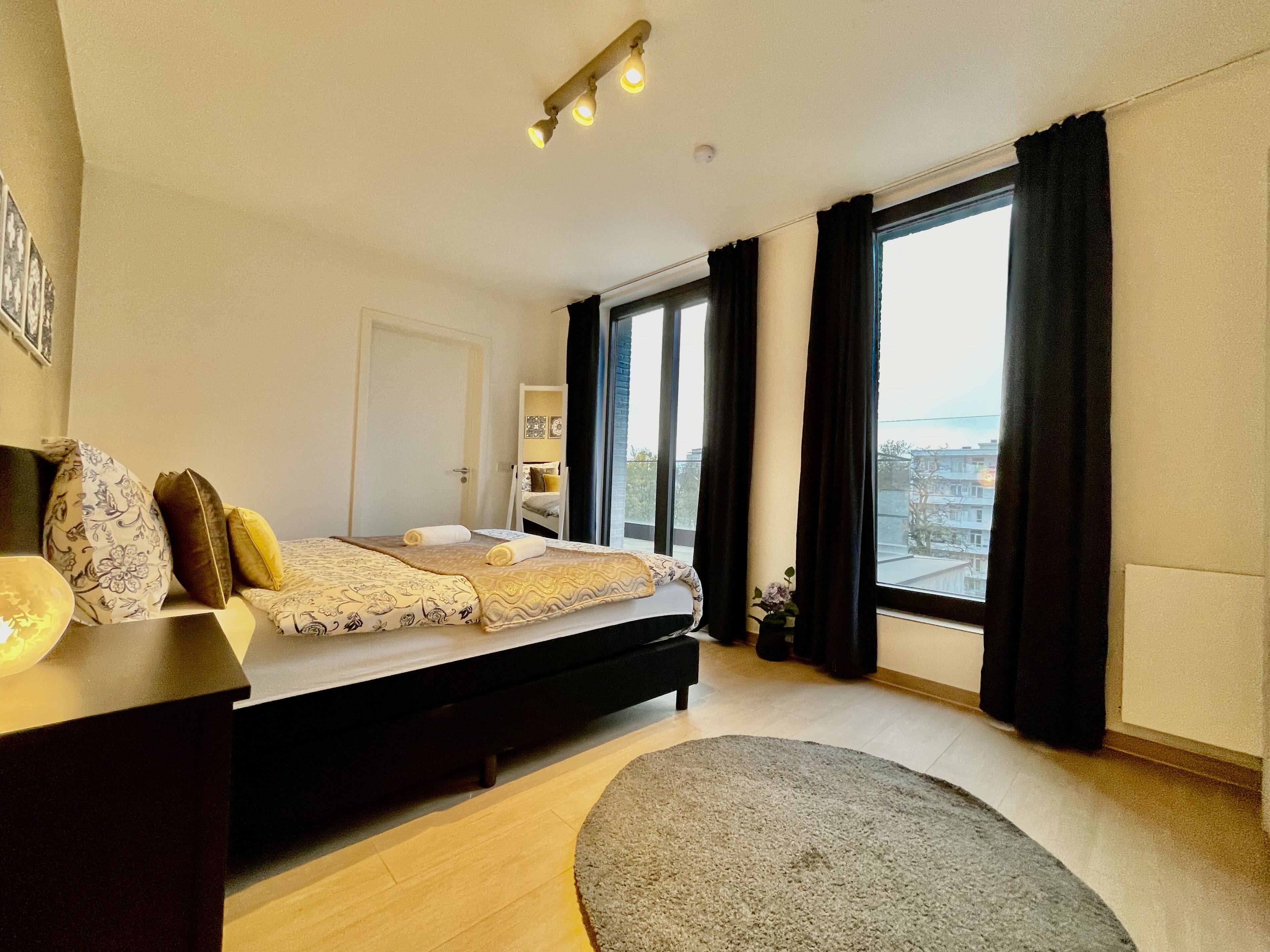 Une chambre moderne avec un lit, une table de chevet et une grande fenêtre avec des rideaux.
