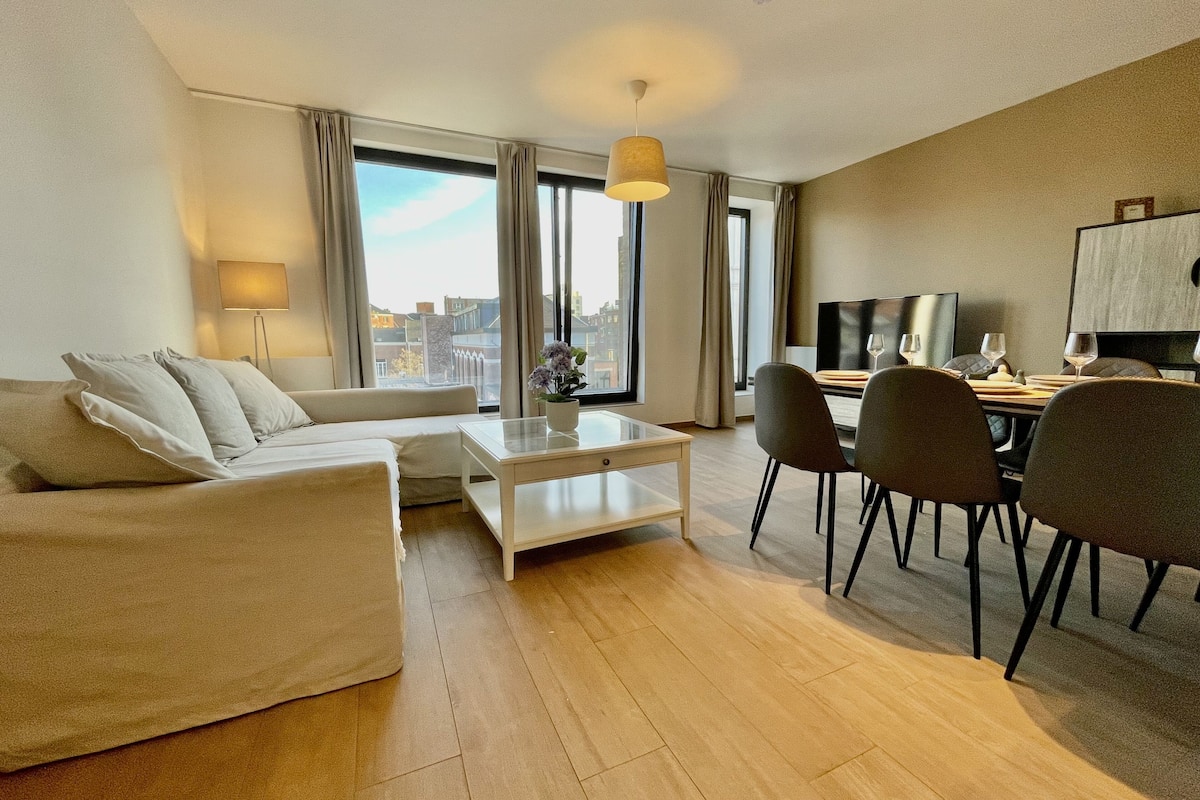 Een moderne woonkamer met een bank, salontafel en een eethoek met stoelen en een televisie.