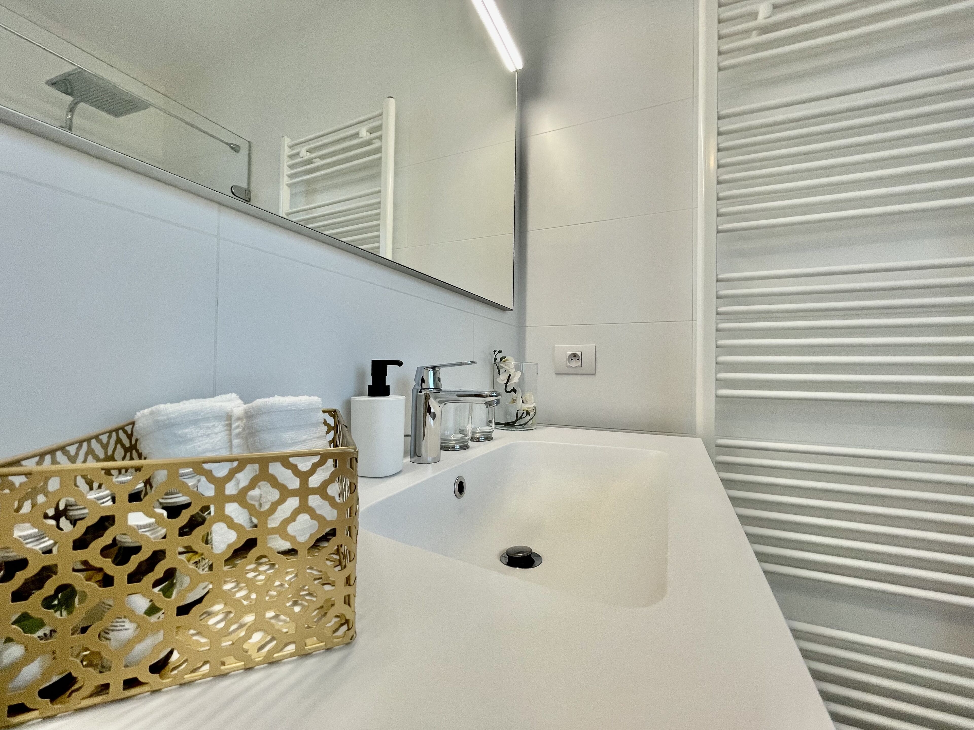 A modern bathroom with a white sink, a mirror, a towel rack, and a decorative basket.