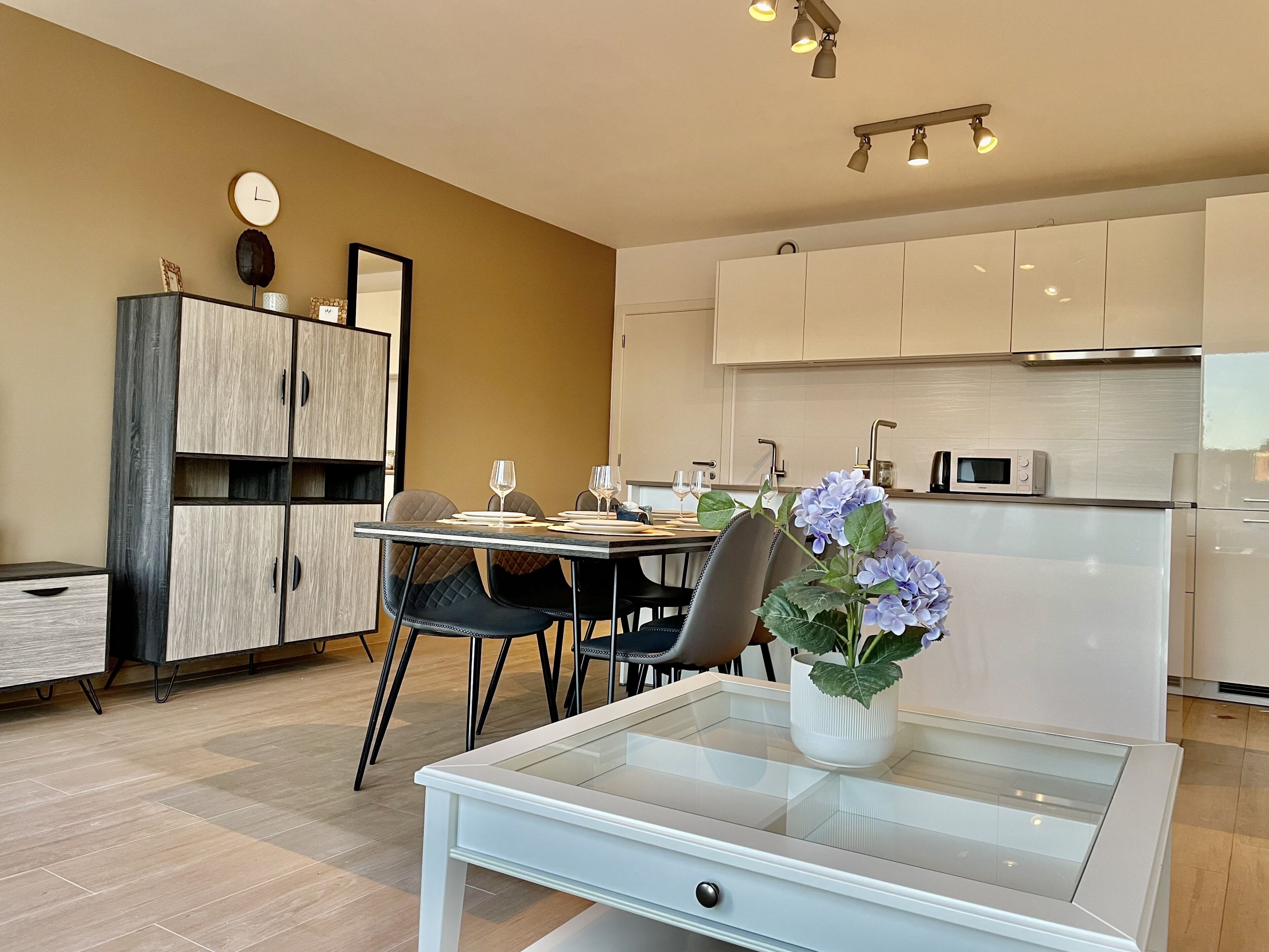A modern kitchen with white cabinets, a dining table with chairs, and a small potted plant.