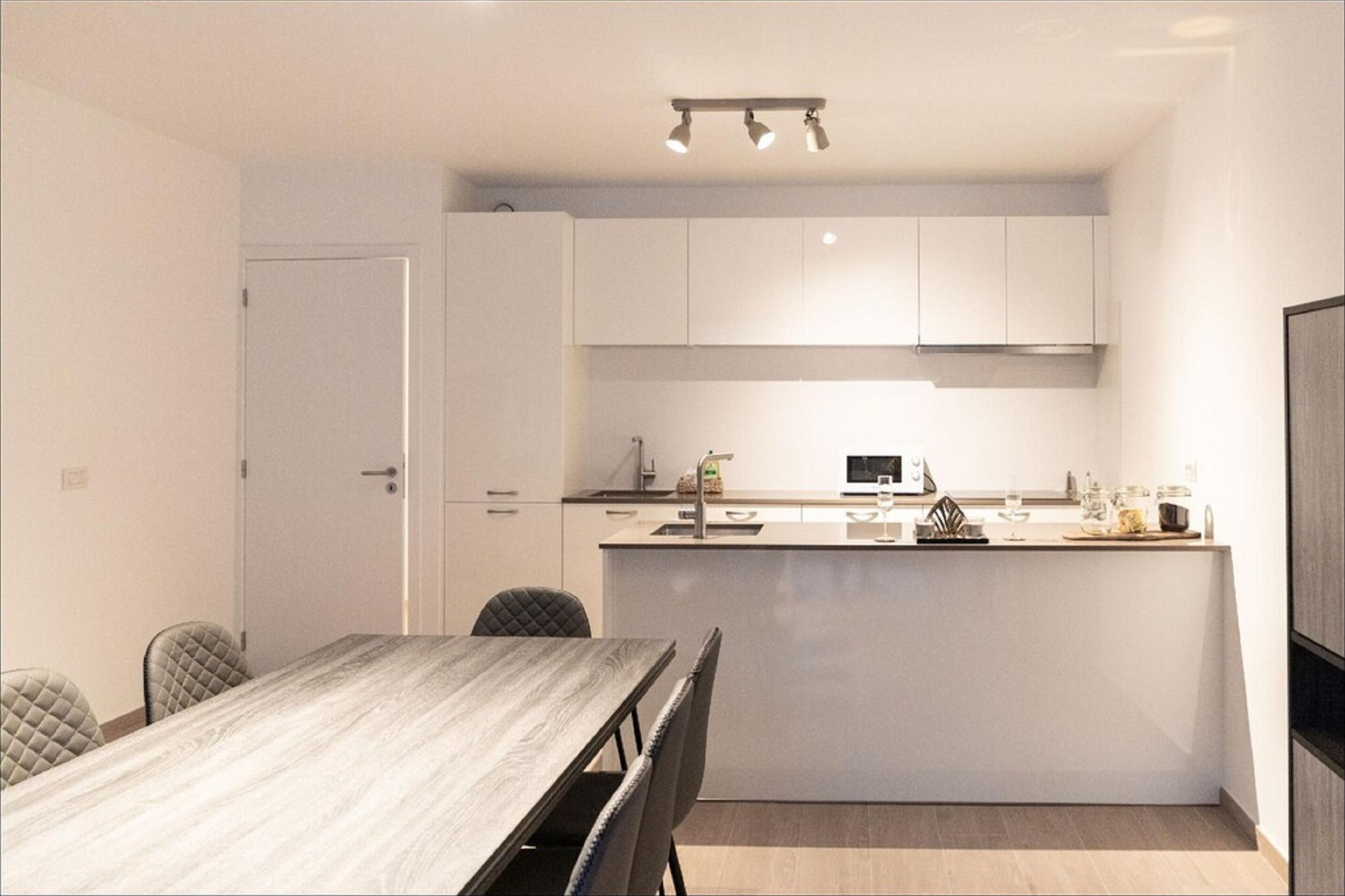 A modern kitchen with white cabinets, a central island, and a dining area with a wooden table and chairs.