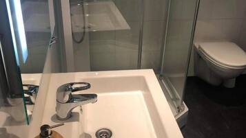 Un baño moderno con ducha envuelta en vidrio, un lavamanos blanco y un dispensador de jabón de madera, y un inodoro.