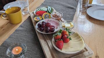 Una mesa de madera con una variedad de alimentos y bebidas, incluyendo platos de uvas, fresas y verduras en rodajas, junto con una taza amarilla y vasos.