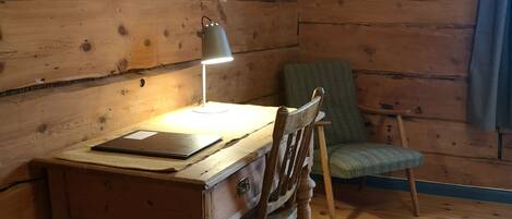 A wooden cabin interior with a desk, chair, lamp, and a window with curtains.