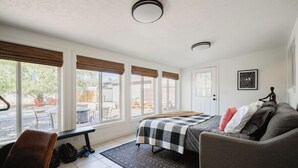 A bedroom with a bed, a gray couch, a bench, and a view of the outside.