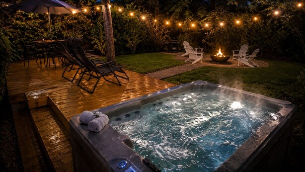 Ein Whirlpool mit Holzterrasse, Gartenstühlen und Lichterketten.