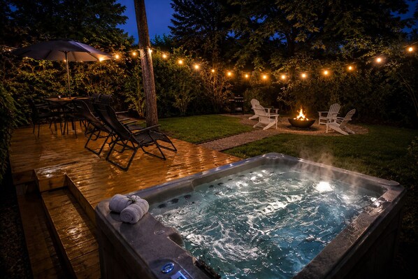 A hot tub with a wooden deck, outdoor chairs, and string lights. - Secluded Cabin w/ Hot Tub • No Neighbors • 15 Min to Texas A&M Aggieland Getaway (Navasota)