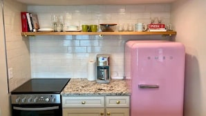 Una cocina compacta con un refrigerador rosa, una estufa y una cafetera sobre la encimera.