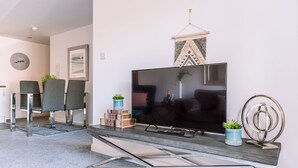 Un soggiorno moderno con una TV a schermo piatto, due poltrone grigie, un tavolino da caffè e oggetti decorativi tra cui una pianta e un pannello decorativo geometrico.