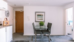 Un'area pranzo moderna con un tavolo in vetro, due sedie, una sveglia e un quadro incorniciato appeso al muro.