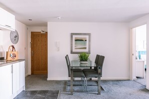 A modern dining area with a glass table, two chairs, a clock, and a framed picture on the wall.