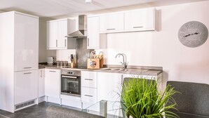Una cucina moderna con mobili bianchi, una cappa in acciaio inossidabile, un forno integrato e un lavello. Si nota un orologio a parete e una pianta nell'angolo.