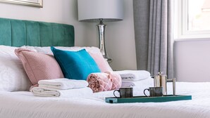 Un letto rifatto con cuscini, una lampada e un vassoio con una tazza e un thermos.