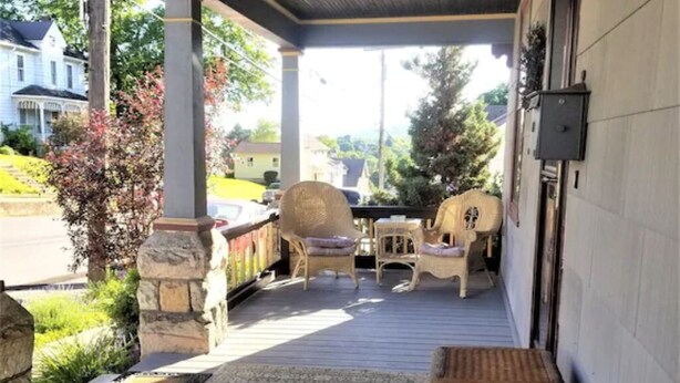 A covered porch with stone pillars, wicker furniture, and a view of a residential street. - Just Like Grandma's House, All Grown Up! (Bellefonte)