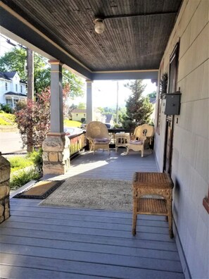 A covered porch with stone pillars, wicker furniture, and a view of a residential street. - Just Like Grandma's House, All Grown Up! (Bellefonte)