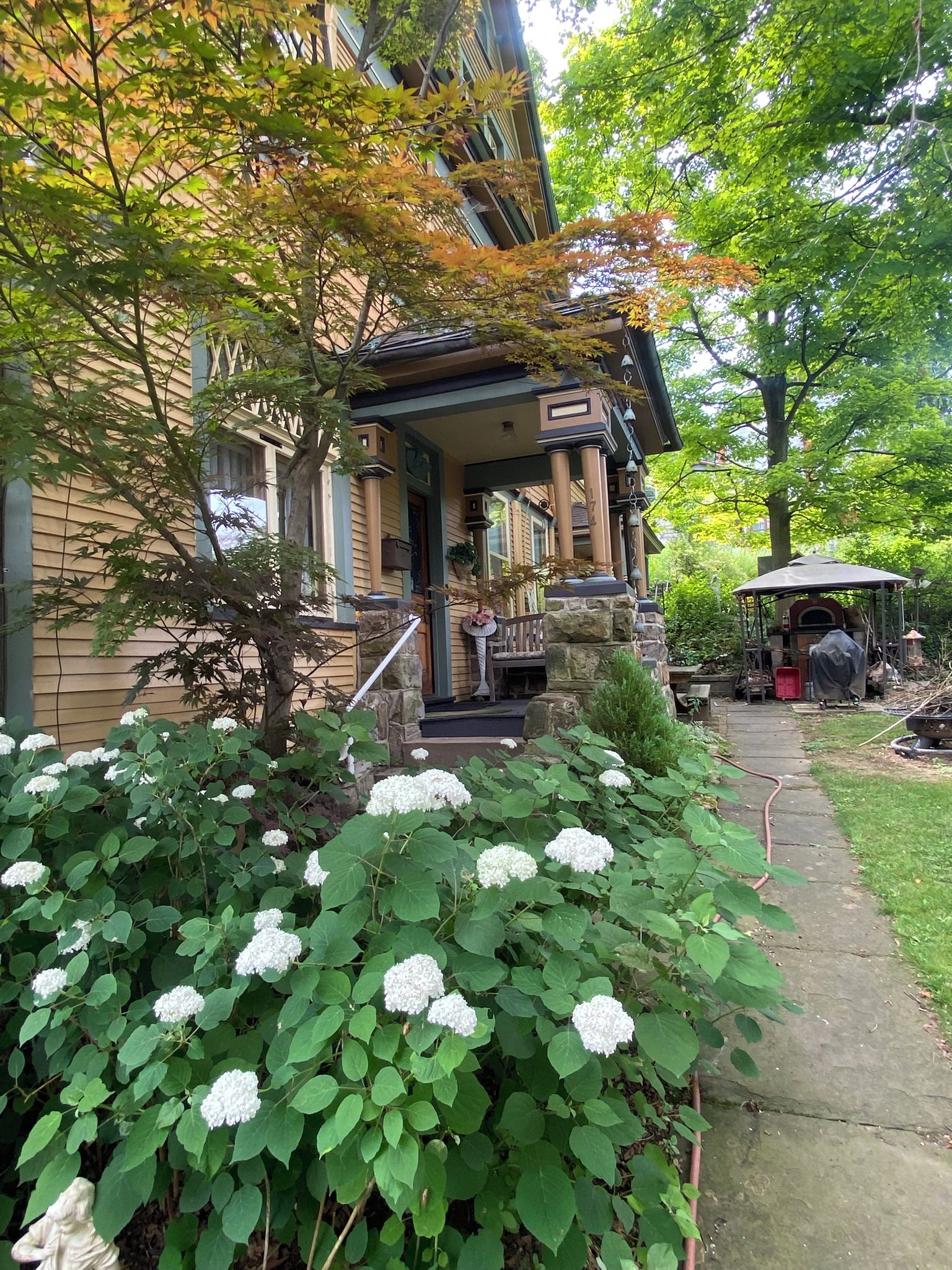 Una casa con porche, columna de piedra y jardín con flores de hortensia.