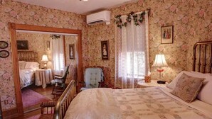 A bedroom with floral wallpaper, a large bed, a chair, a small table, and an air conditioning unit.
