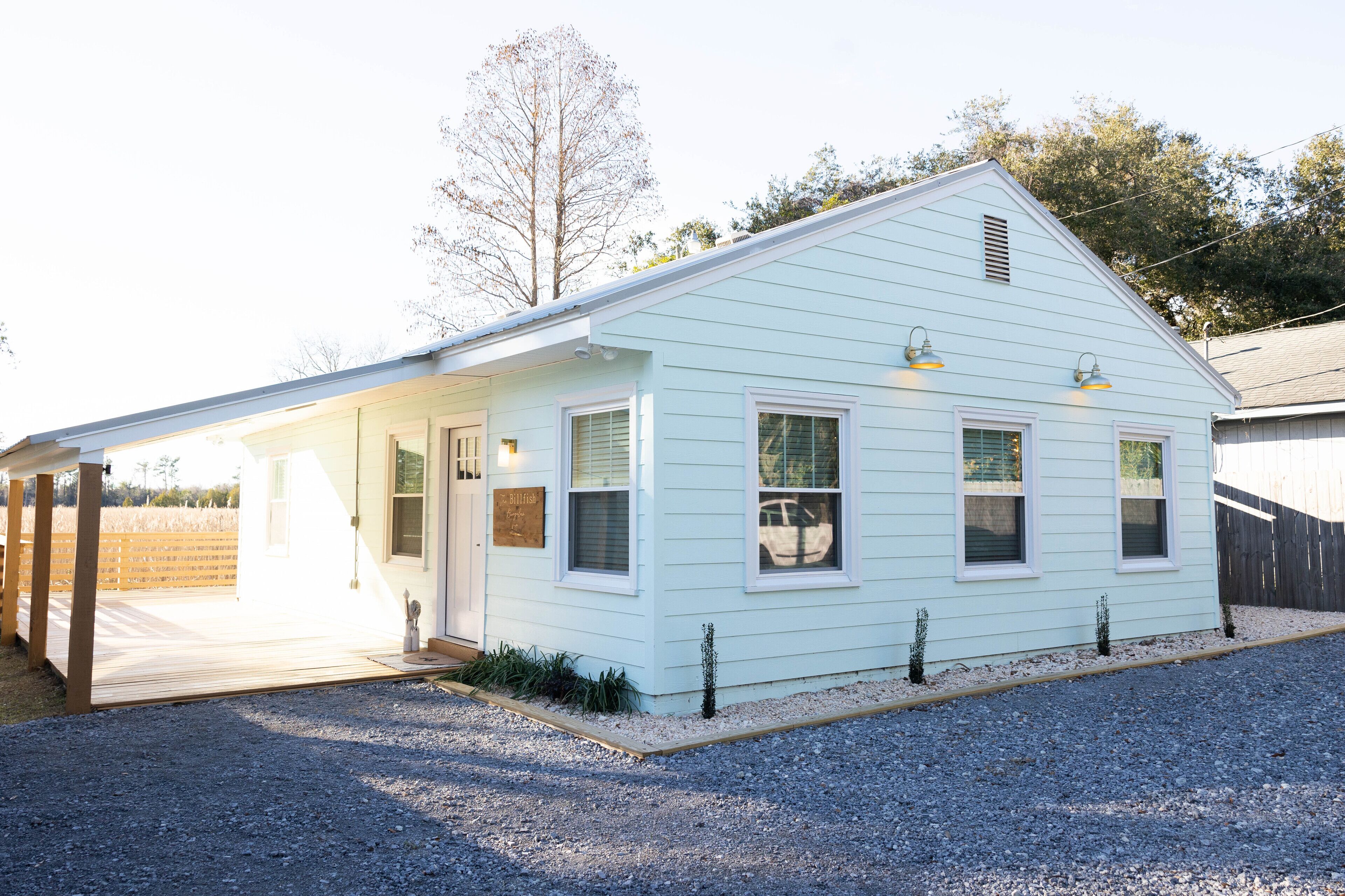 A light blue single-story house with a covered porch, a small front yard, and a gravel driveway.