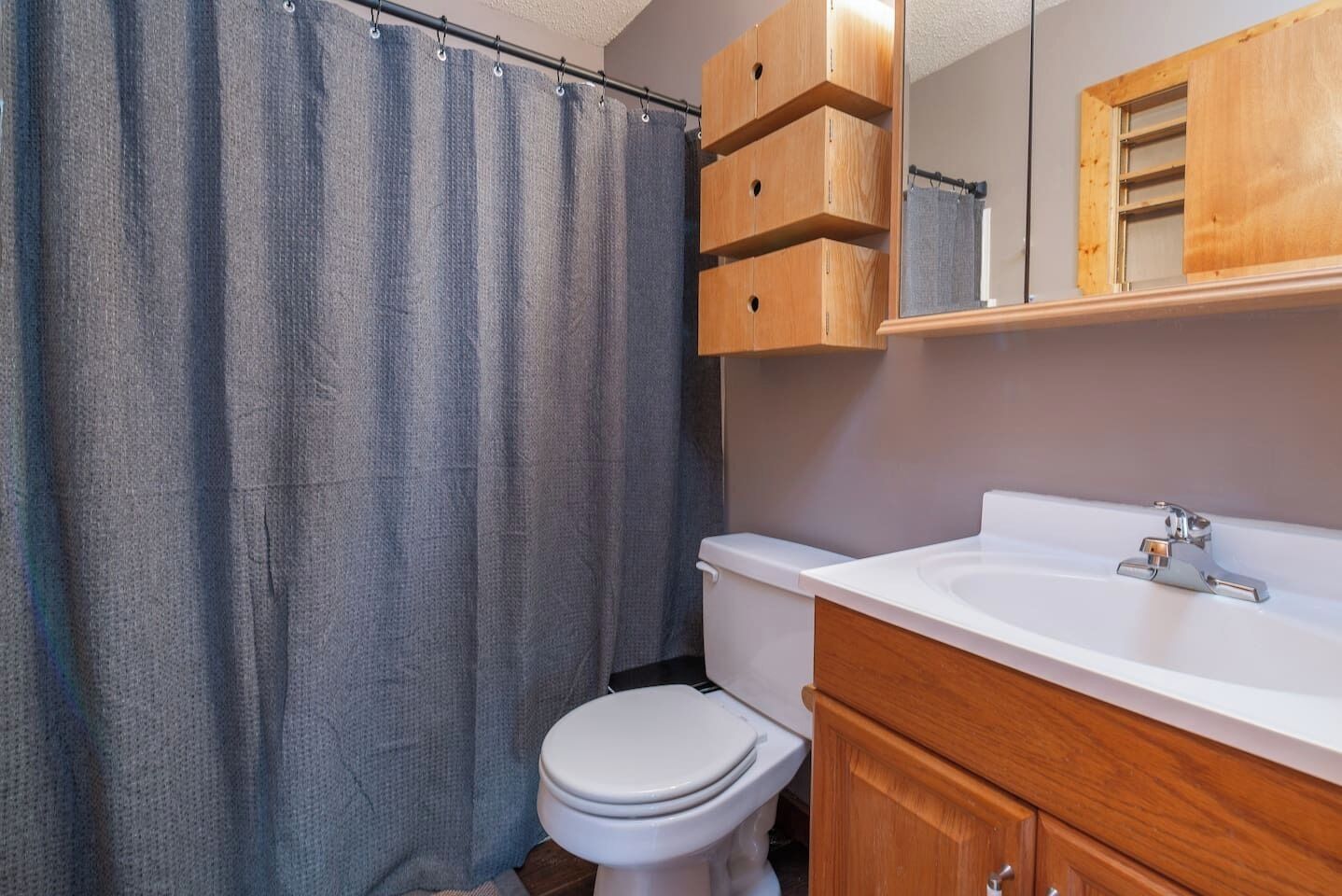 Un baño con cortina de ducha, inodoro, lavamanos y armarios de madera.