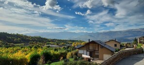 A residential area with houses, a stone wall, and a view of distant mountains under a partly cloudy sky.