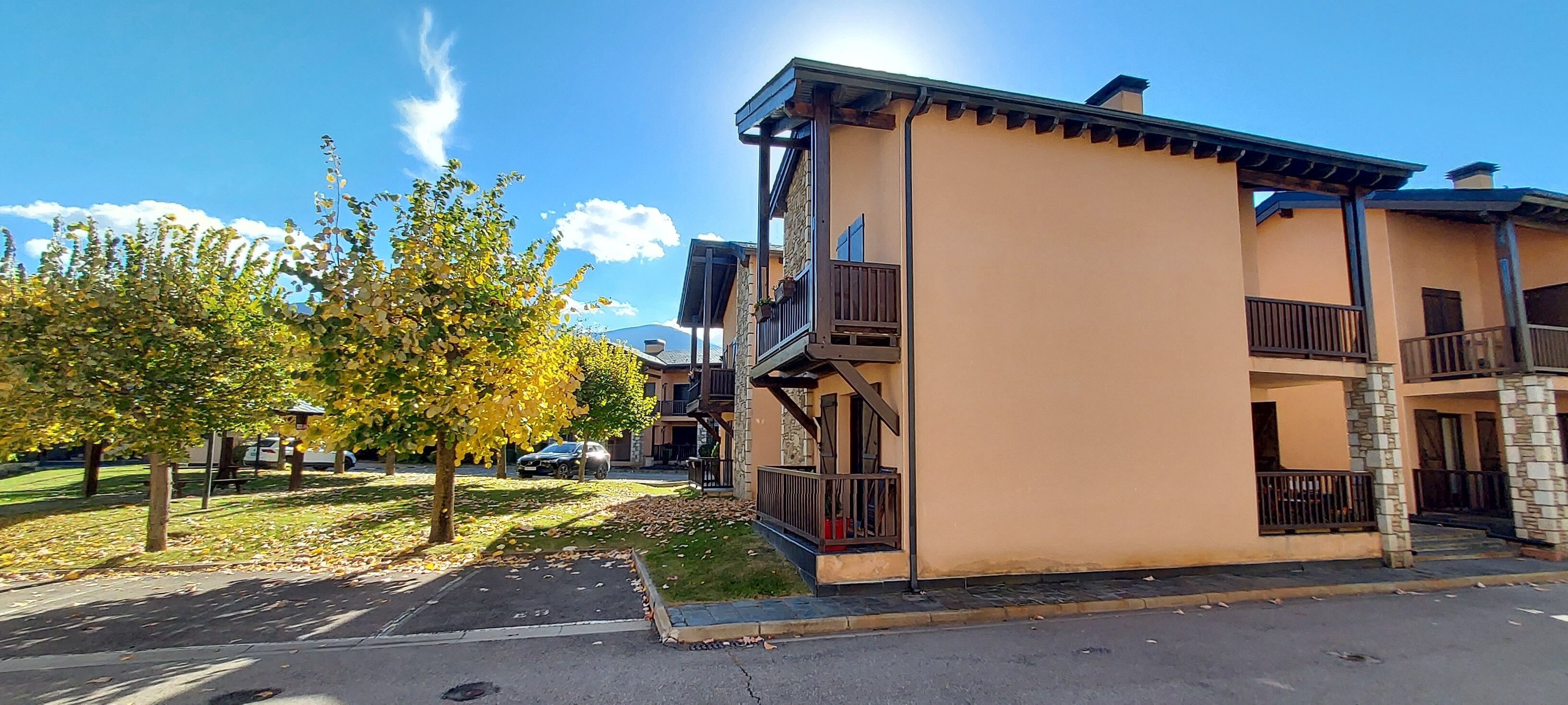 A two-story building with balconies, a parking lot, and a tree with yellow leaves.