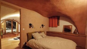 A bedroom with a curved ceiling, a bed, a bedside table, and a mirror. - Les Voûtes (Champcella)