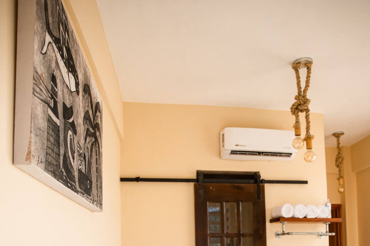 A hotel room with two beds, a wooden headboard, a wall-mounted air conditioner, and a framed picture.