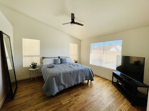 A bedroom with a bed, a ceiling fan, a TV, and windows.