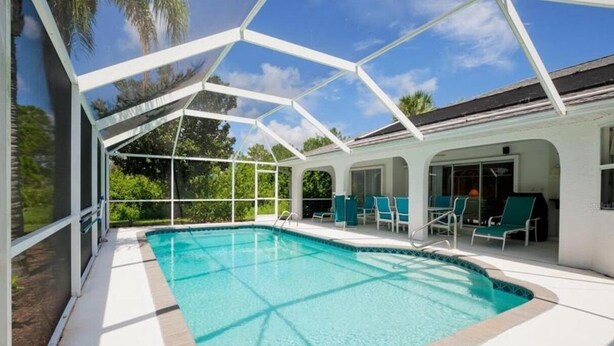 A covered swimming pool with clear blue water, surrounded by white walls and a glass enclosure. - Single family pool home in a quiet neighborhood, close to five beaches,  (Port Charlotte)