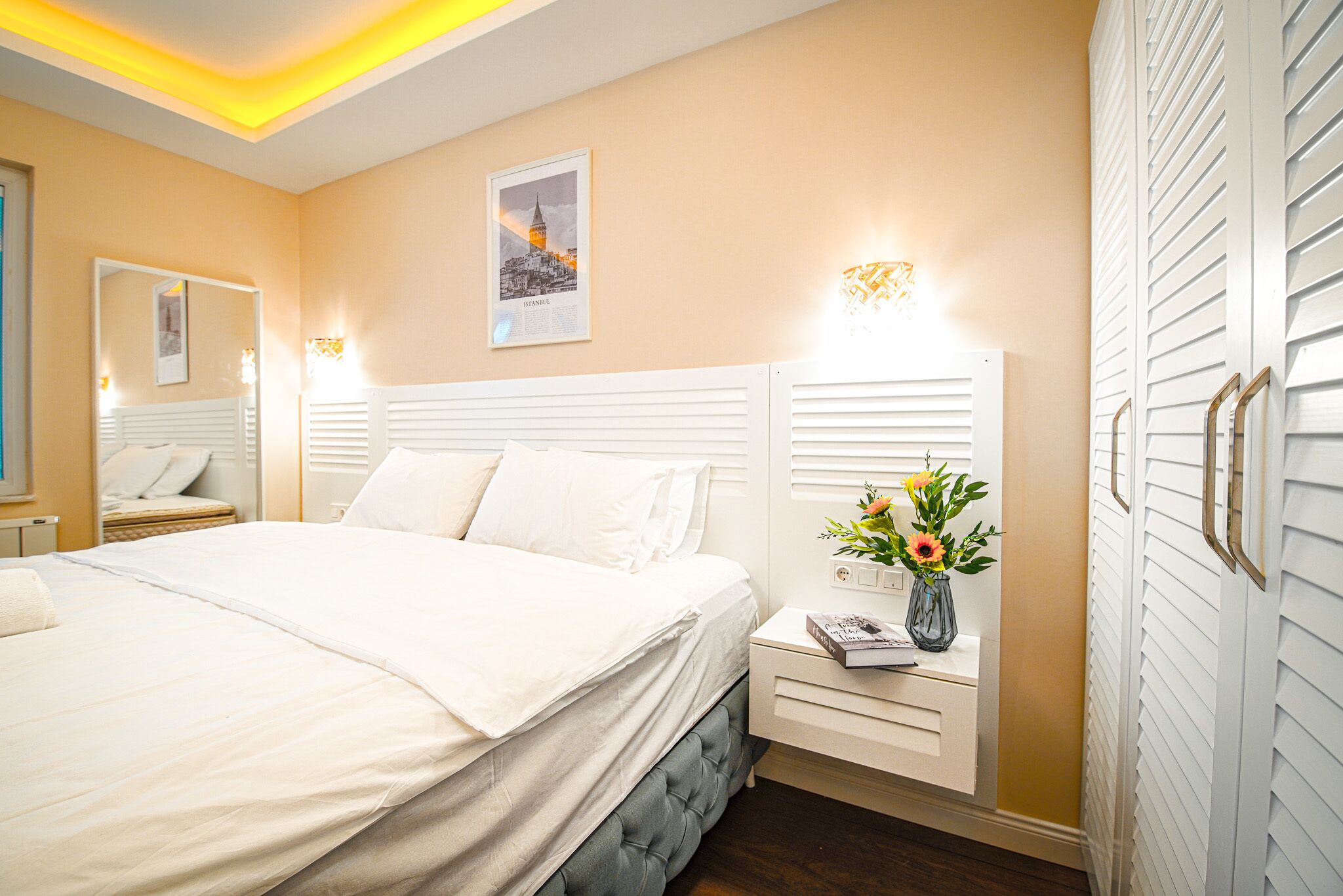 A bedroom with a large bed, bedside tables, a nightstand with a vase of flowers, and a framed picture on the wall.