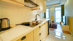 Una cocina moderna con estufa, lavamanos y armarios. Se ve una ventana con cortinas y un televisor al fondo.