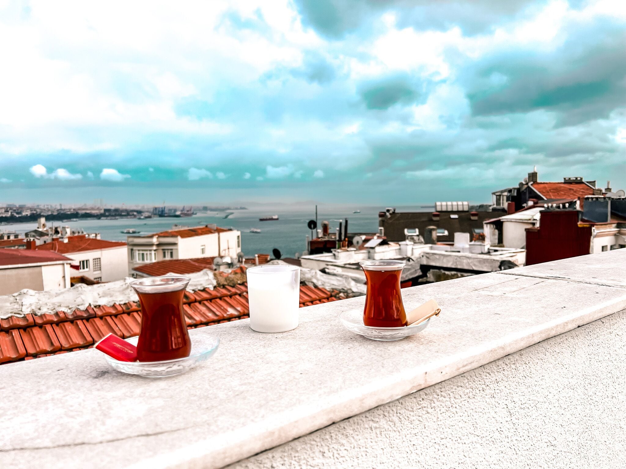 Una terrazza con due bicchieri di tè e una tazza bianca, con vista su un paesaggio urbano che include edifici e una distesa d'acqua.