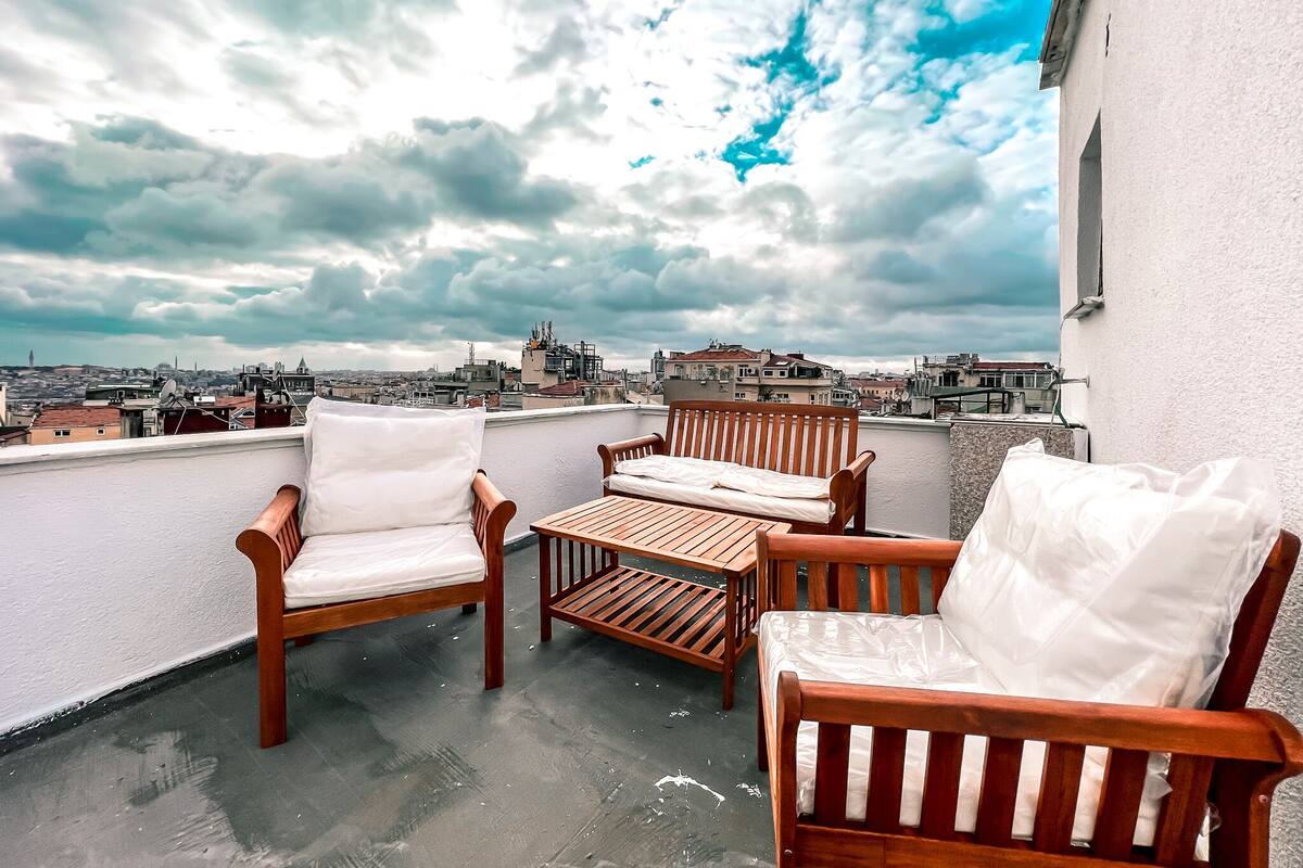 A rooftop terrace with wooden furniture and a view of the cityscape.