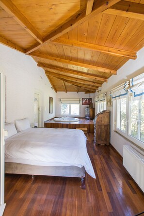 Un dormitorio con techo de madera, una cama, un aparador de madera, una ventana con cortinas y un radiador.