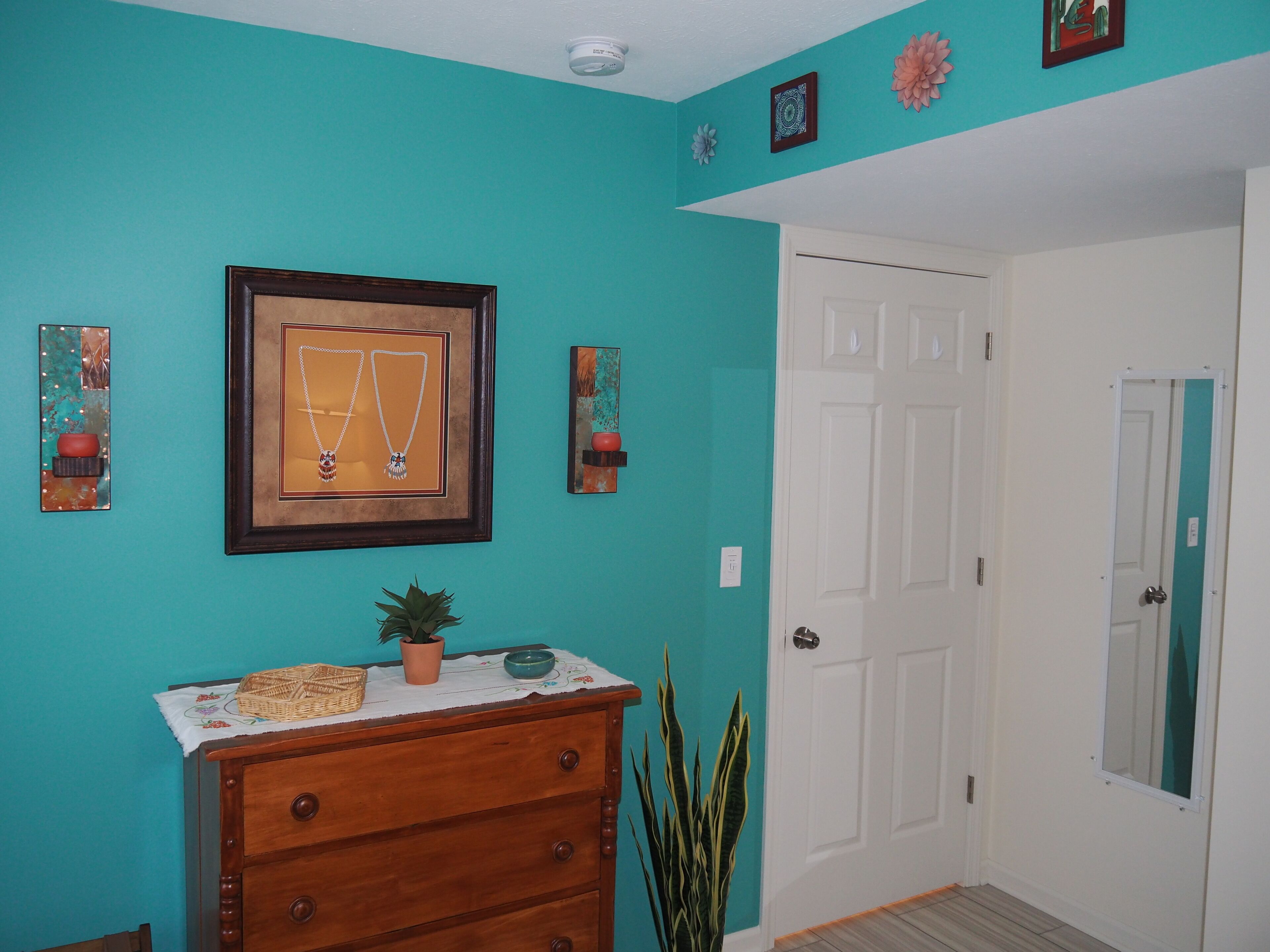 Een kamer met teal muren, een houten dressoir, een lijst met sieraden, een deur en een kamerplant.