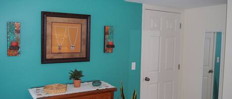 Een kamer met teal muren, een houten dressoir, een lijst met sieraden, een deur en een kamerplant.