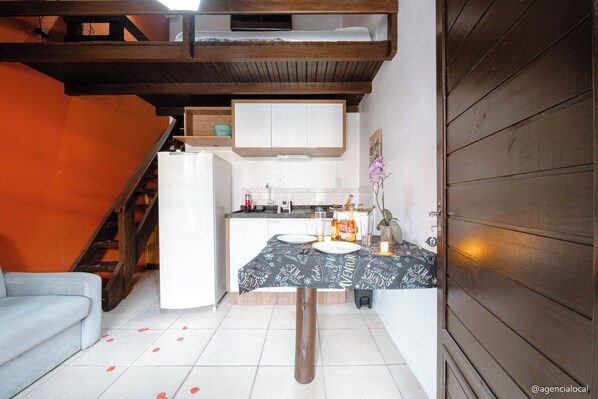 A compact kitchen with a white refrigerator, a dining table set with plates, and a small island with a candle. - POUSADA REFUGIO DO ROSA (Imbituba)